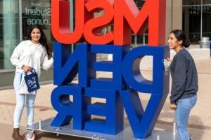 Two students standing next to a big "MSU DENVER" sign outside of the Jordan Student Success Building.